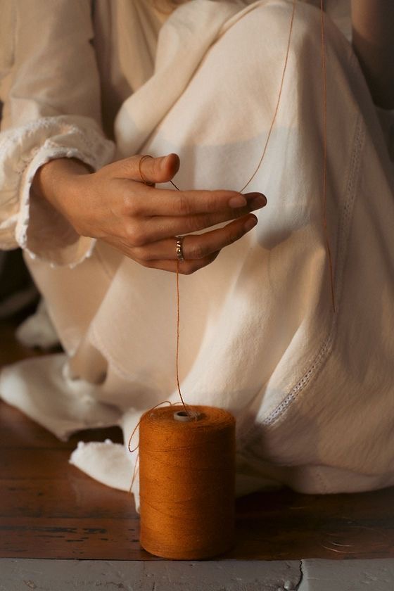 An artisan guiding fine thread by hand beside a spool
