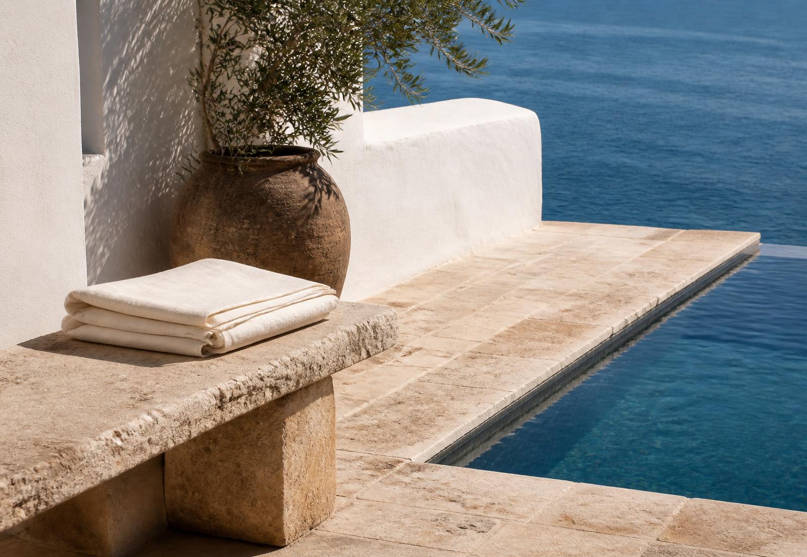 Folded cream cotton cloth on a travertine bench beside a still pool
